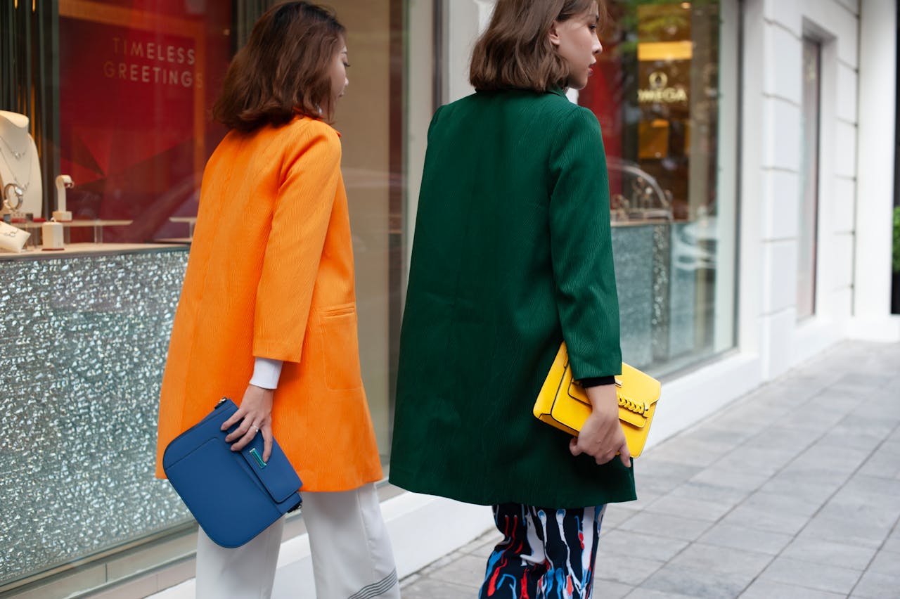 Mastering the First Impression: Your intriguing post title goes here Two women in colorful coats walking past luxury storefronts, showcasing modern street fashion.